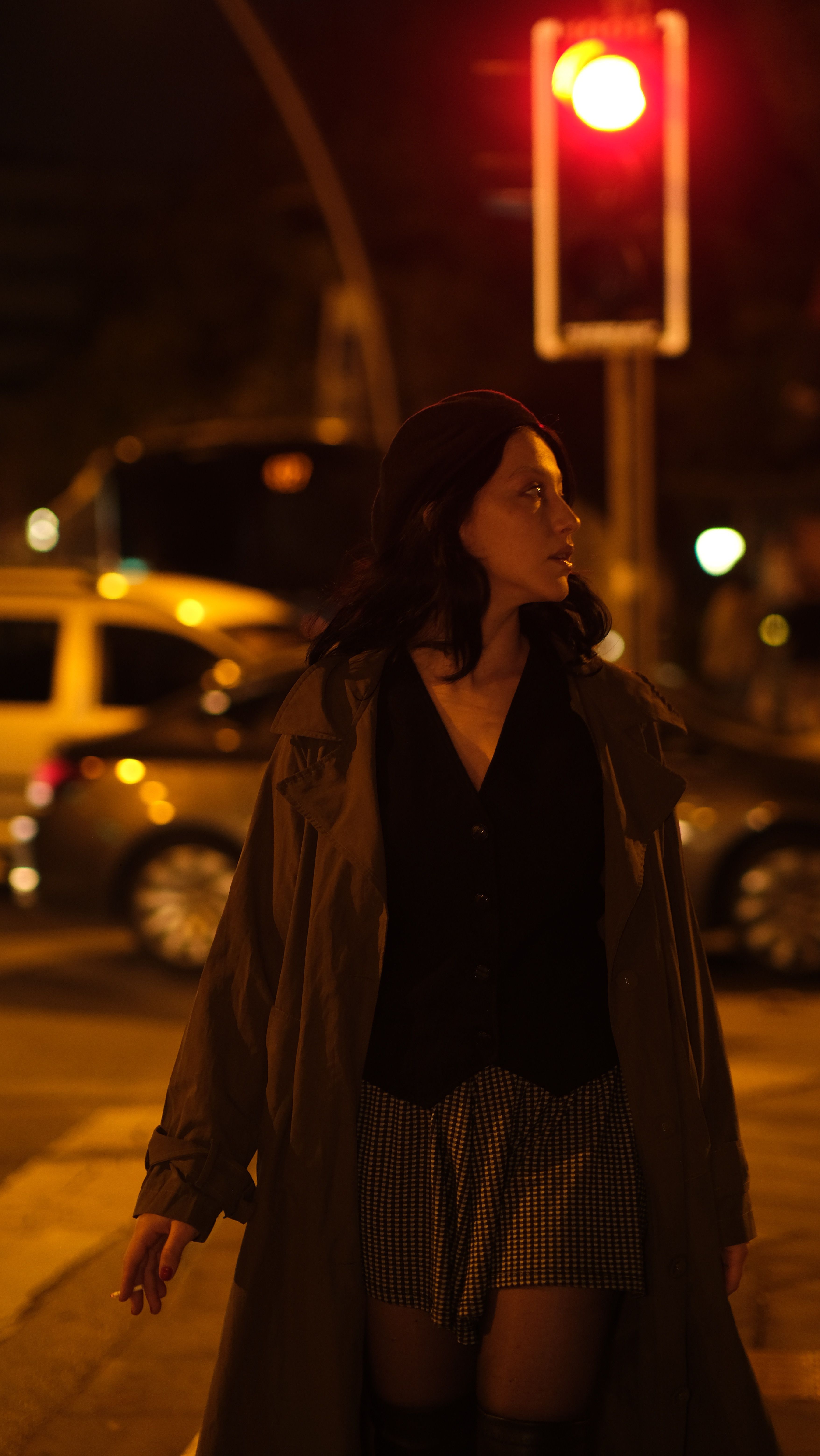 Woman walking in city at night under red traffic light, urban atmosphere.