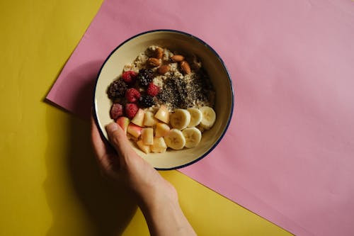 Close-up of a Person Holding a Bowl of Oats with Fruits and Nuts 