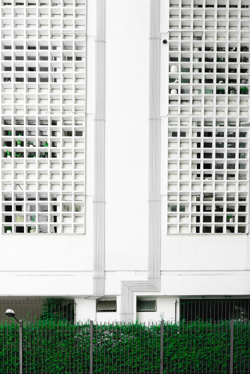 Detailed view of a modern geometric building facade with greenery at the base, showcasing symmetry and contemporary design.