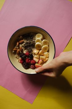 A nutritious bowl of oatmeal topped with fruits, nuts, and seeds on colorful background.