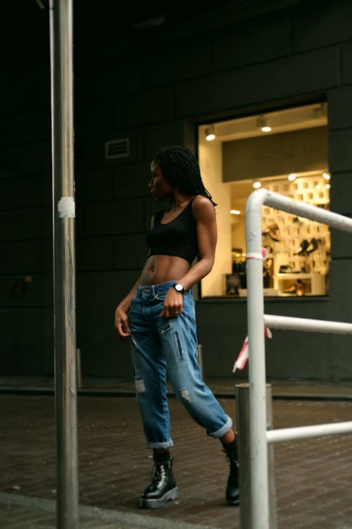 彼女のジーンズを保持している黒いクロップトップで店の前を横切って立っている女性の写真