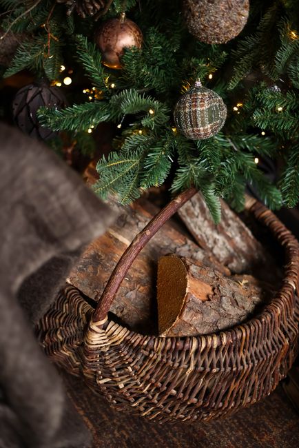 Detailed shot of firewood in a wicker basket beneath a decorated Christmas tree with baubles.