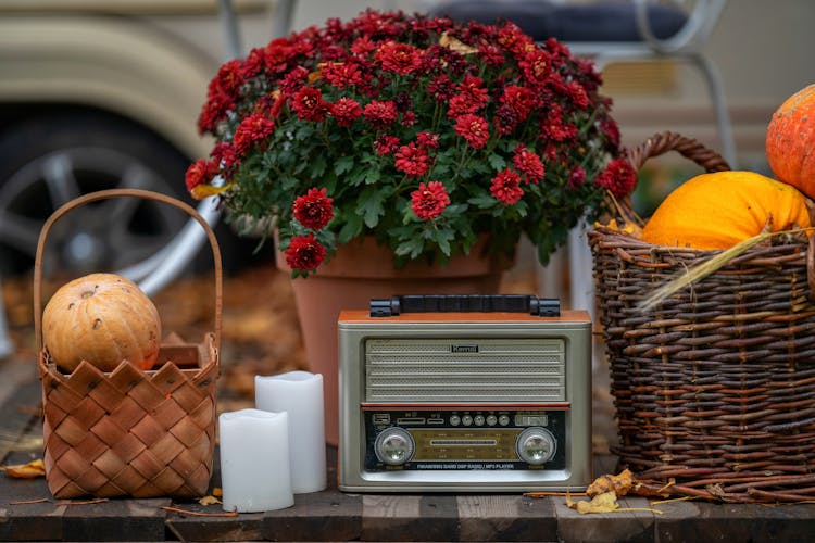 Retro Radio Set Next To Pot Of Red Flowers And Baskets Of Fruits