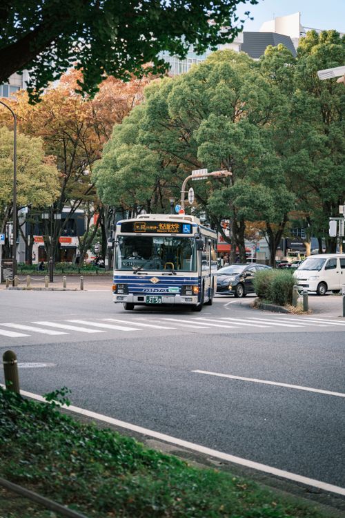 Free A public bus turns at a city intersection surrounded by trees and buildings, capturing urban commute. Stock Photo