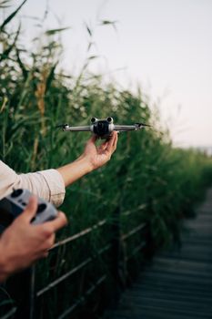 Man holding a hovering drone near a boardwalk, showcasing modern technology outdoors.