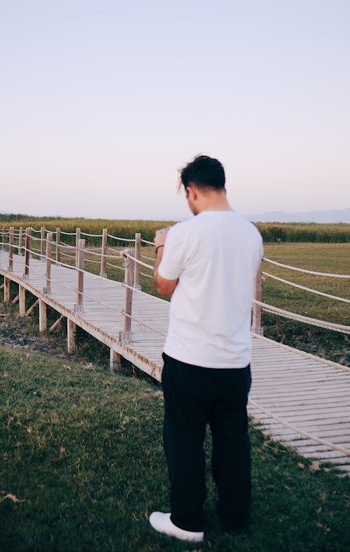 Man in White T-shirt Standing by Wooden Footpath