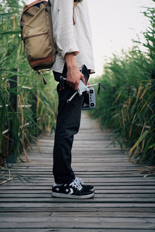 Man with a Backpack and a Drone Standing on a Boardwalk 