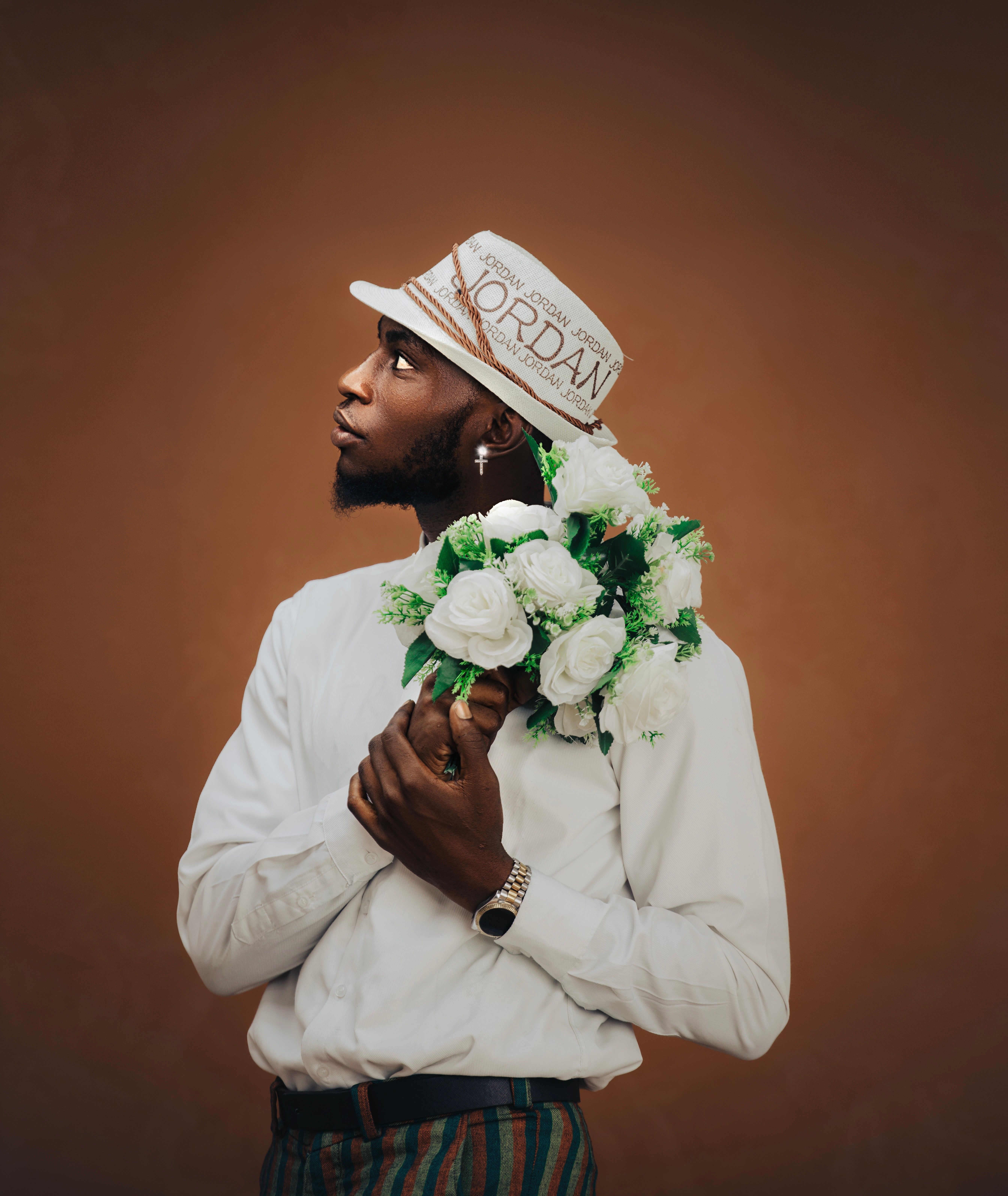Side profile of a stylish man holding a bouquet of white flowers in a studio setting. Elegant and poised.