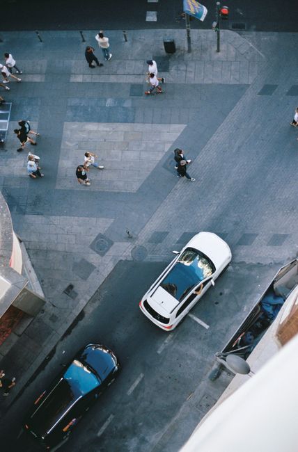 Aerial view of urban street with cars and pedestrians on a sunny day.