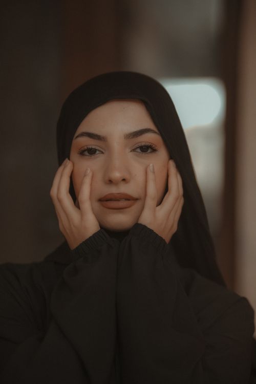 Free Serene portrait of a young woman in a black hijab with hands on face, exuding calmness and confidence. Stock Photo