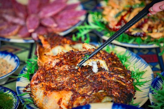 Close-up of spiced grilled fish with chopsticks and salad on a vibrant plate.