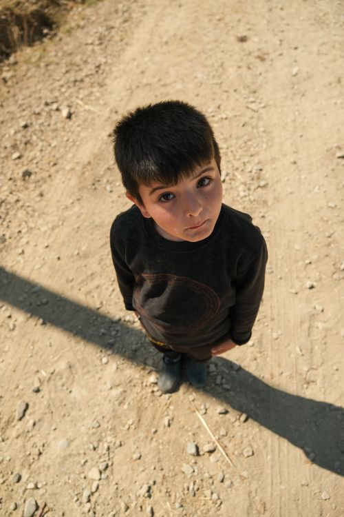 Free Cute boy standing on a rural dirt road, gazing upwards with curious expression. Stock Photo