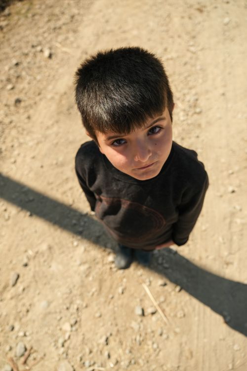 Free High-angle shot of a young boy looking up on a sunny road, exuding innocence and curiosity. Stock Photo