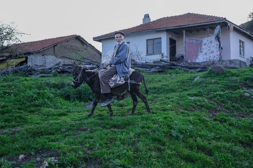 Free An elderly man riding a donkey through a rural countryside with traditional houses in the background. Stock Photo