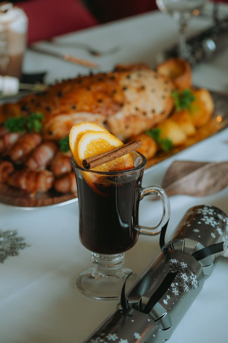 A Drink With Lemon Slices And Cinnamon Stick Standing On A Table With A Christmas Cracker And Food 