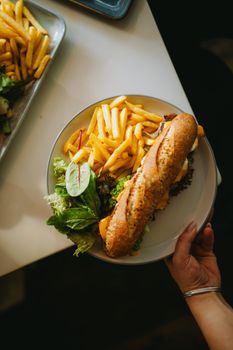 Top view of a fresh sandwich with fries and salad on a plate, ready to eat.