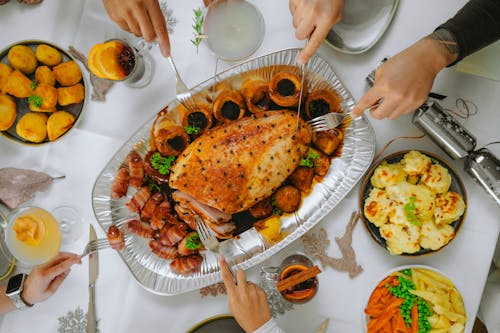 People Cutting Roasted Meat during a Meal Together