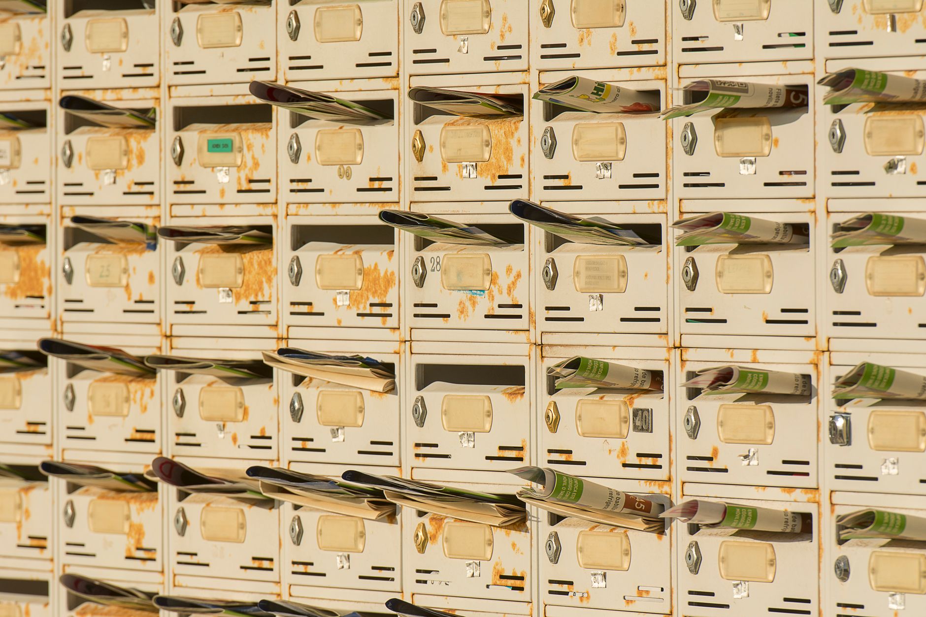 A row of rustic metal mailboxes stuffed with newspapers, creating a vintage urban vibe.