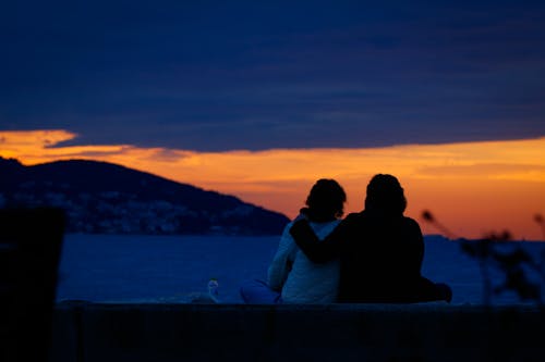 Couple Sitting on Sea Shore at Sunset