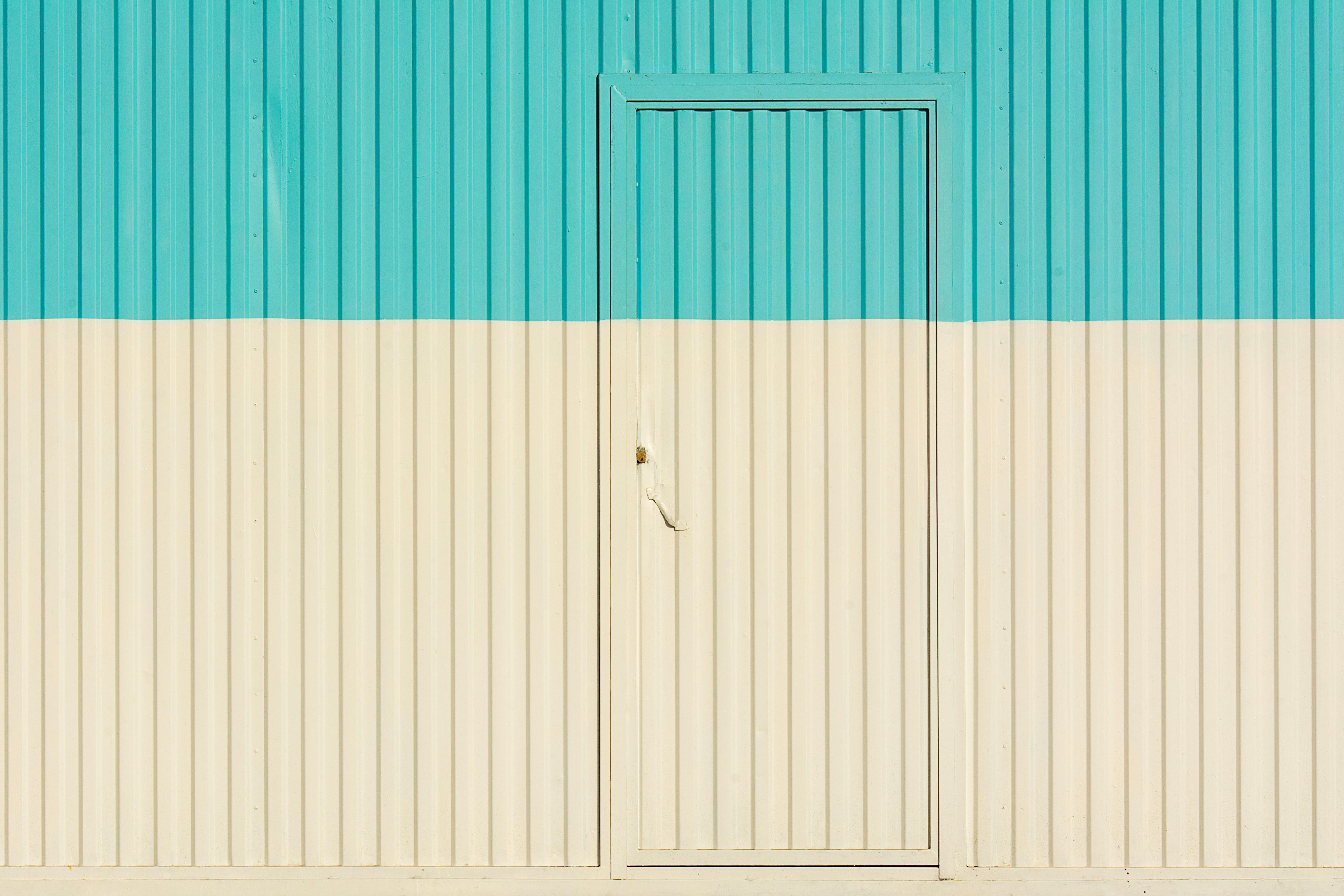 A minimalist image depicting a blue and white sheet metal wall with a single door.