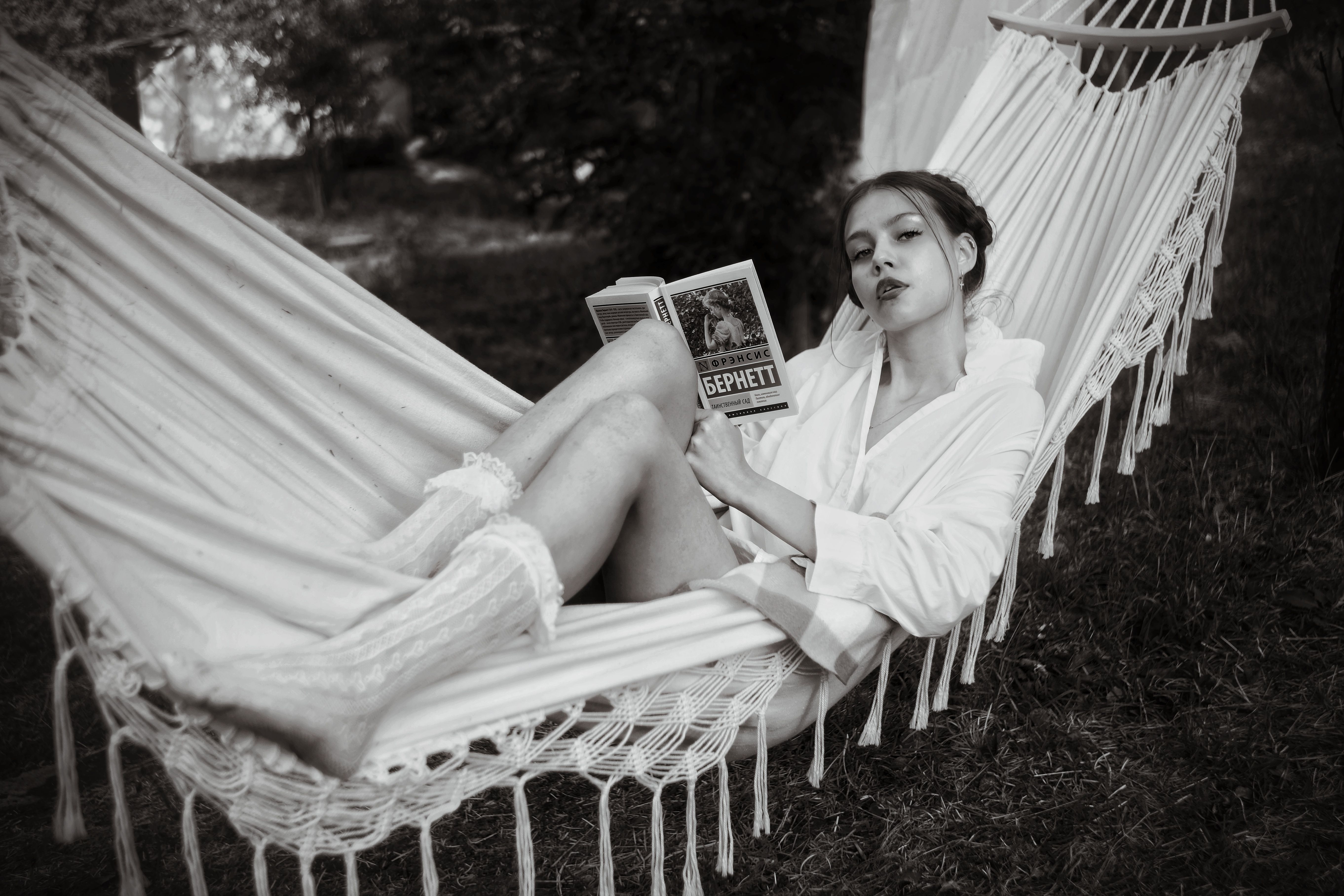 A woman enjoys leisure time reading a book while lying in a hammock outdoors.