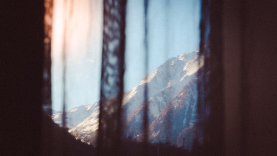 Serene view of snow-covered mountain through a delicate lace curtain.