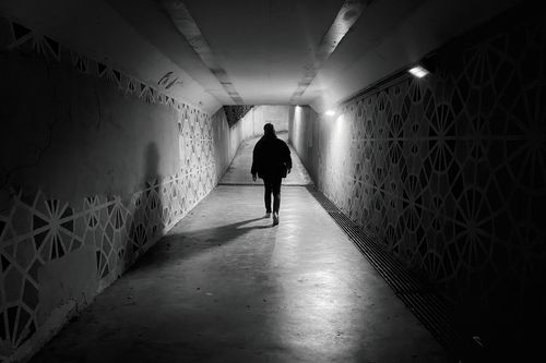 Free A lone figure walks through a geometrically patterned urban tunnel in black and white. Stock Photo