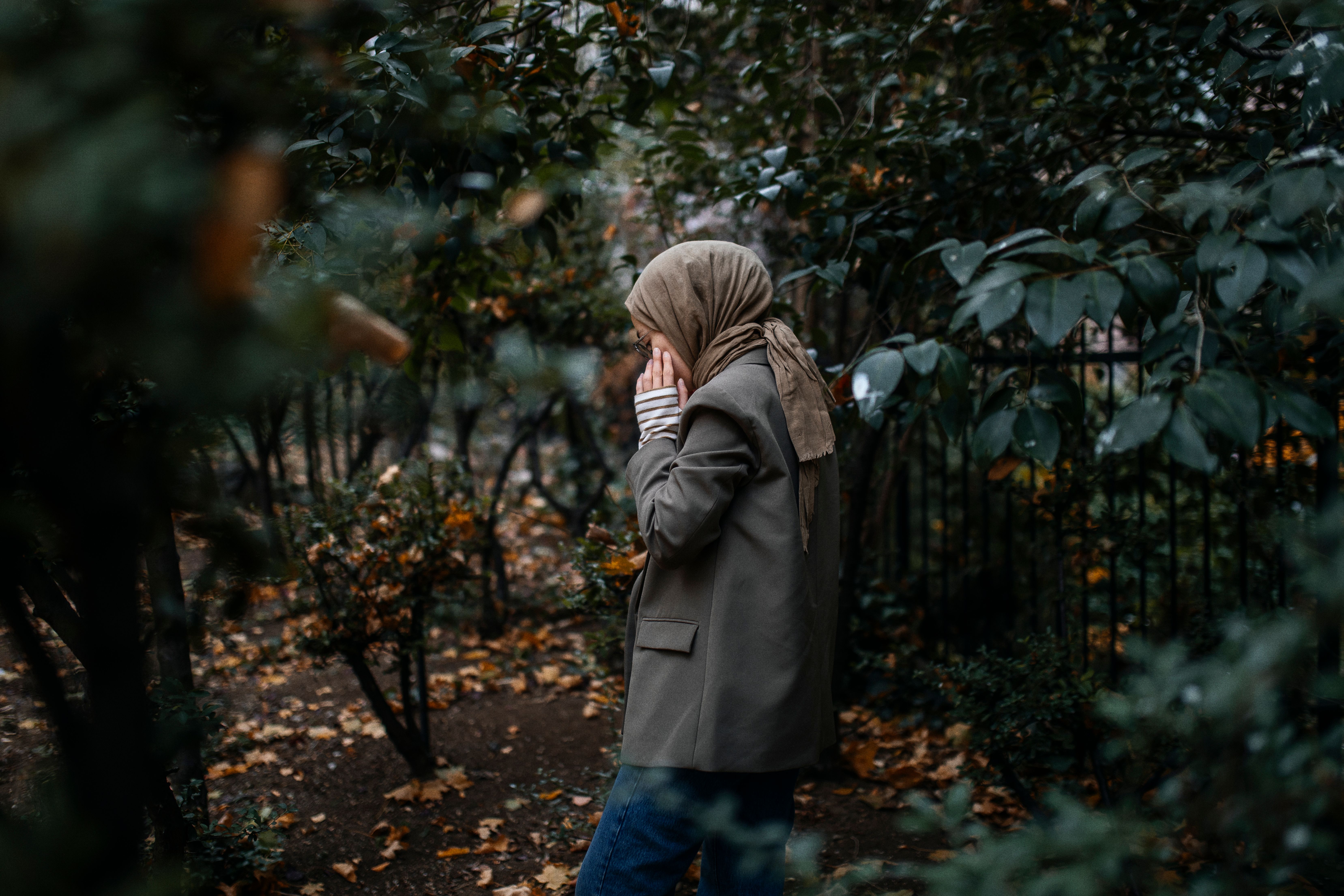 A woman wearing a hijab walks thoughtfully through a leafy autumn park.