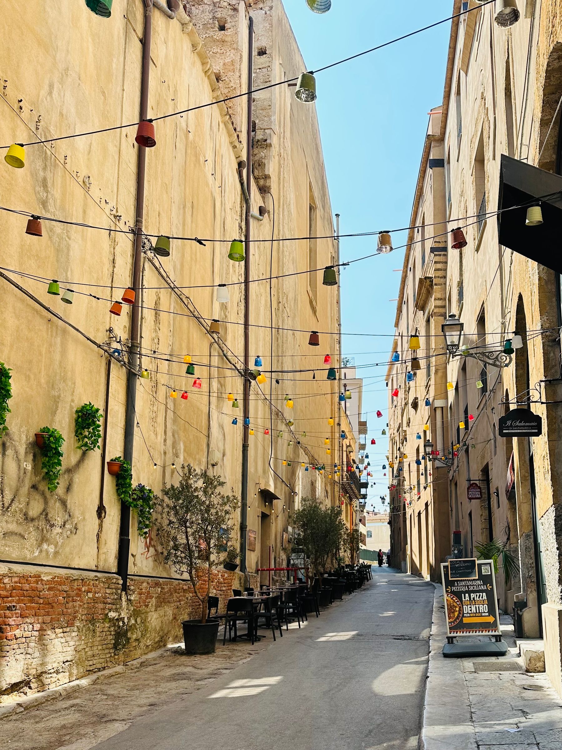 Un vicolo di Palermo a mezzogiorno, muri di intonaco scrostato color sabbia e file di lampadine colorate tese fra i palazzi
