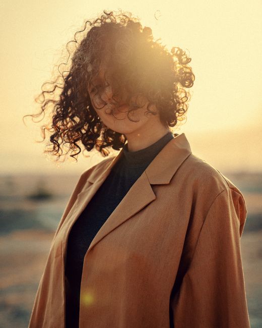 A serene portrait of a woman with curly hair backlit by a warm sunset.