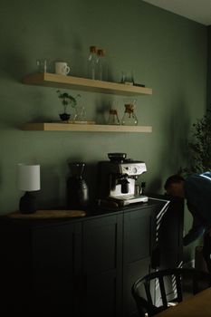 A modern kitchen corner with a coffee machine, shelves, and a person organizing.