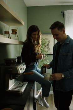 A happy couple making coffee with a machine in their cozy kitchen setting.