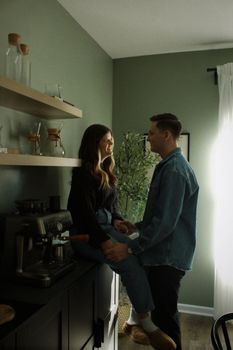 A couple shares an intimate moment near a coffee machine in a cozy kitchen setting.