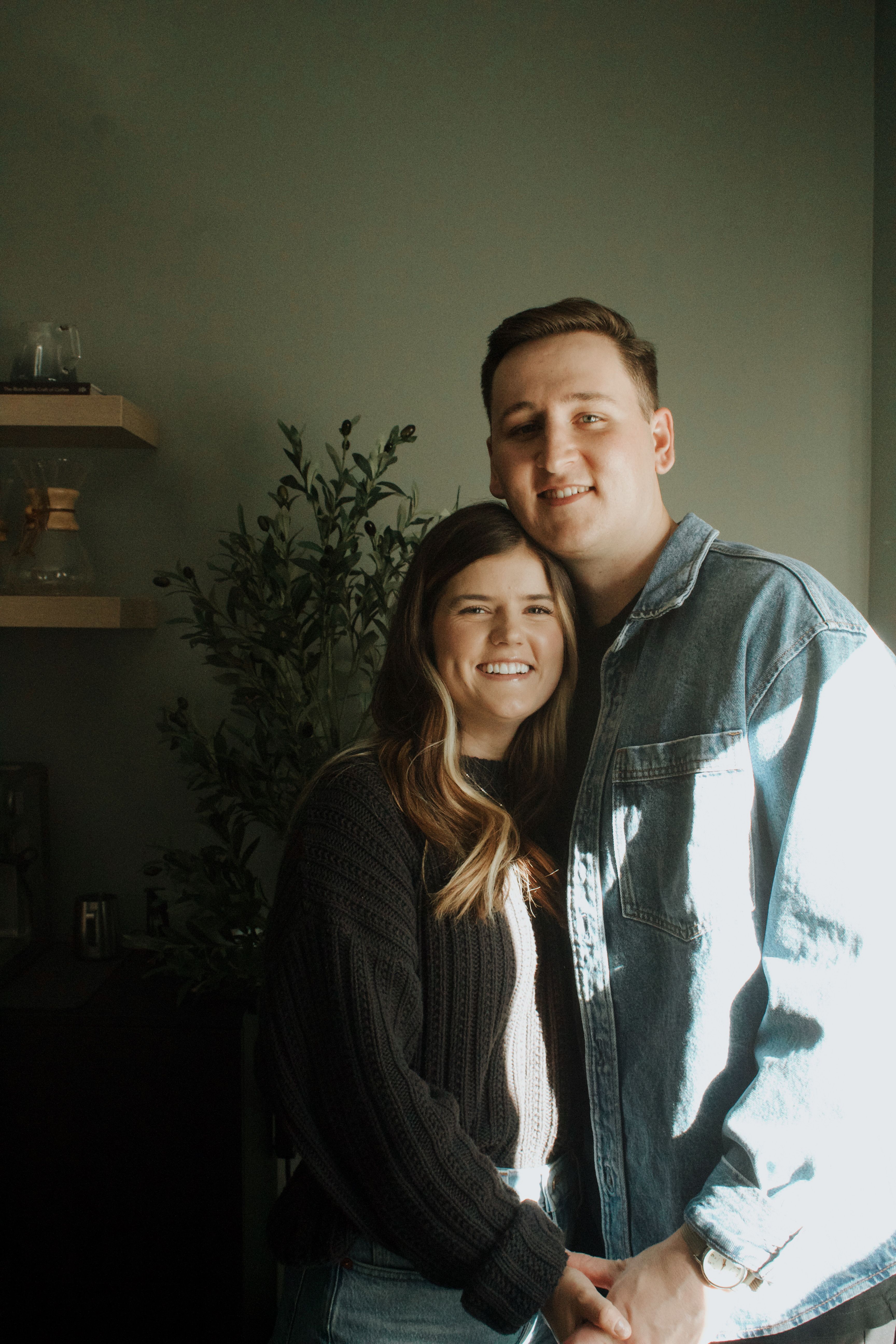 Young couple smiling and embracing in a cozy indoor setting, basking in warm natural light.