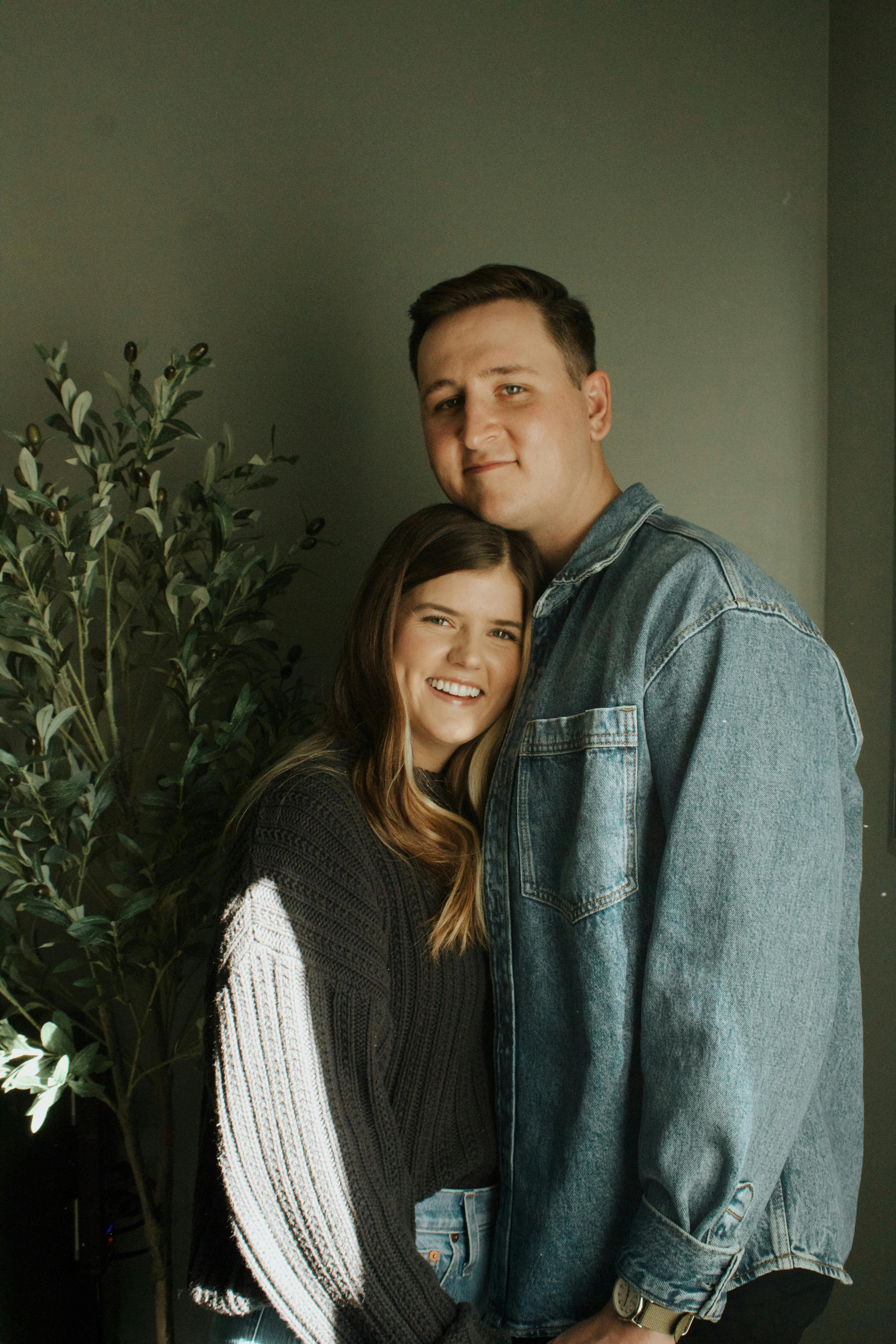 A young couple embracing indoors with a green background, showcasing love and warmth.