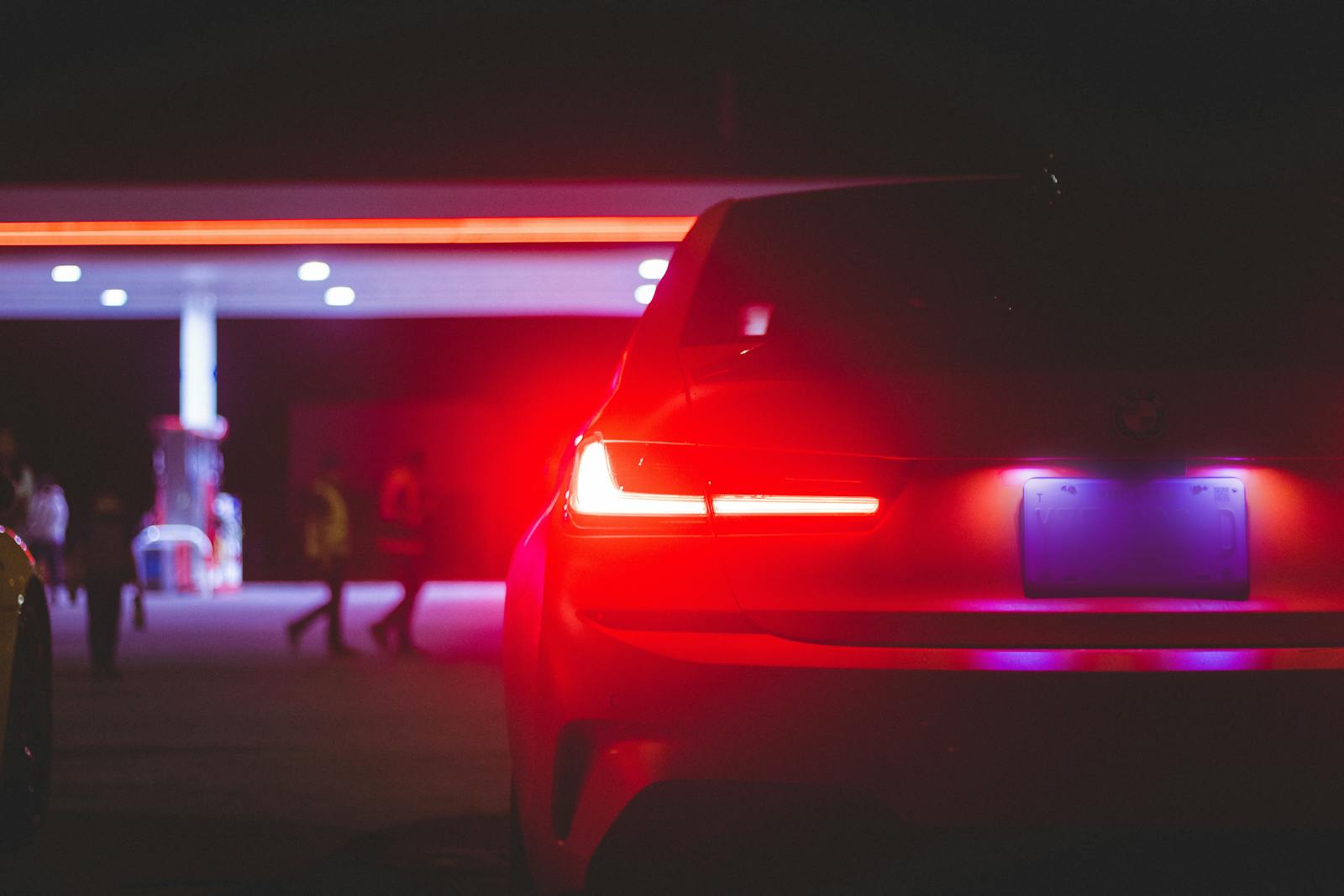 Car taillights glowing at night with soft bokeh near a gas station canopy
