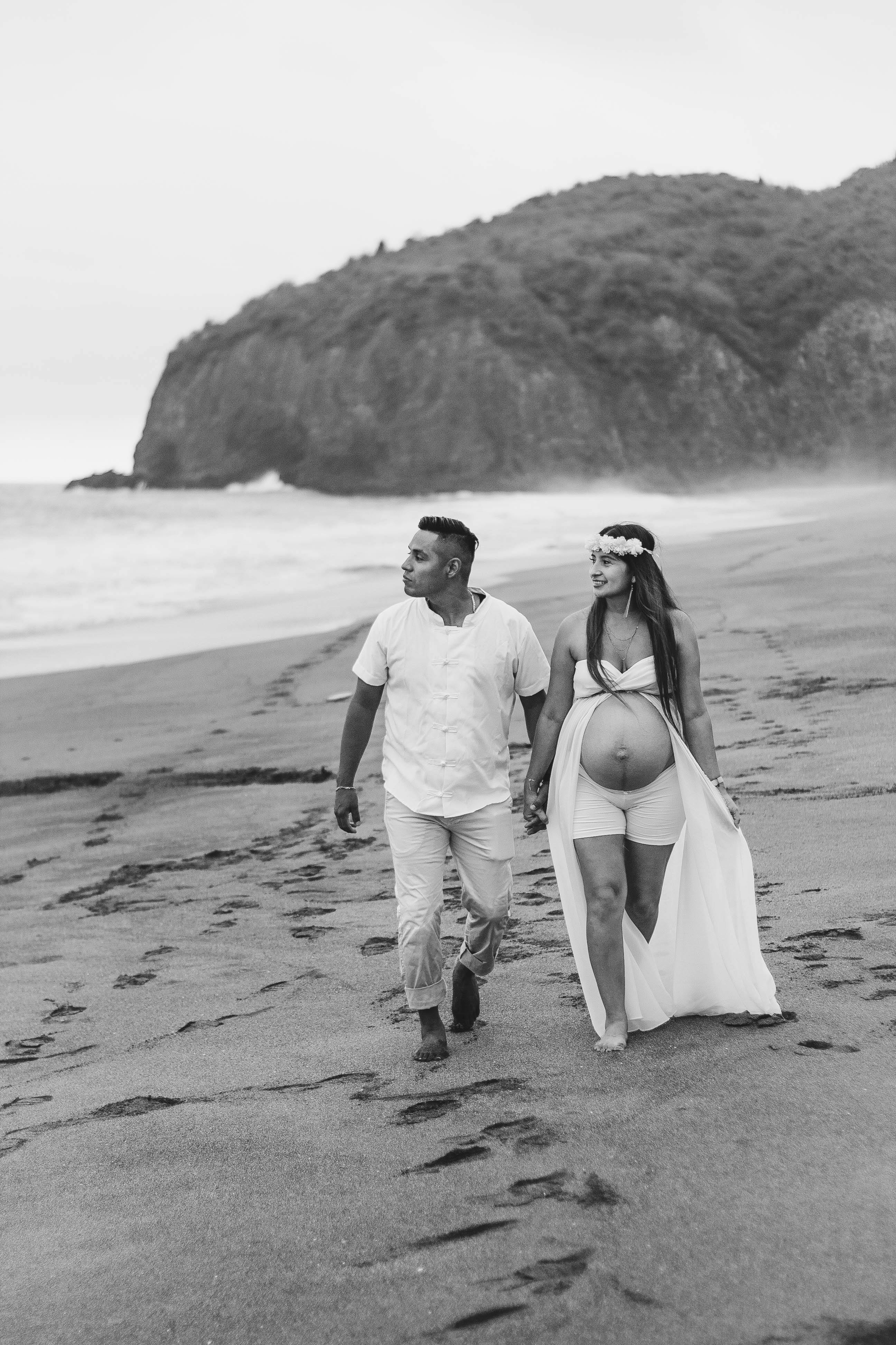 A couple walking along the beach in a serene black and white maternity photoshoot.