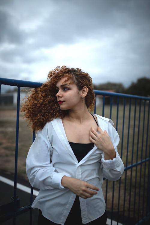 Young Woman in a White Blouse by the Fence on a Windi Day