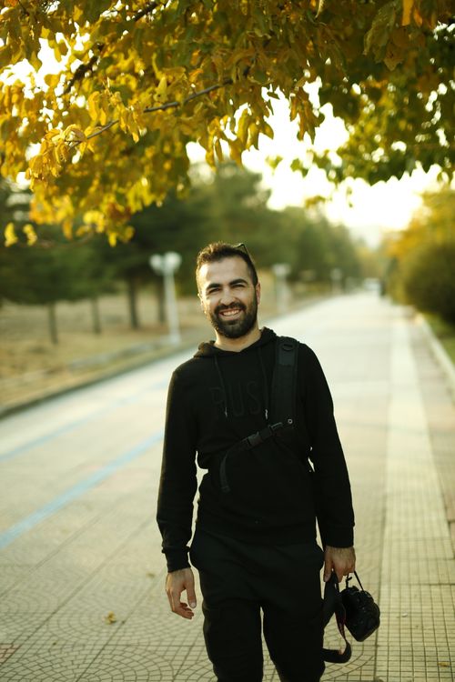 Free A smiling man with a camera enjoys a stroll in the park during fall, showcasing vibrant autumn colors. Stock Photo