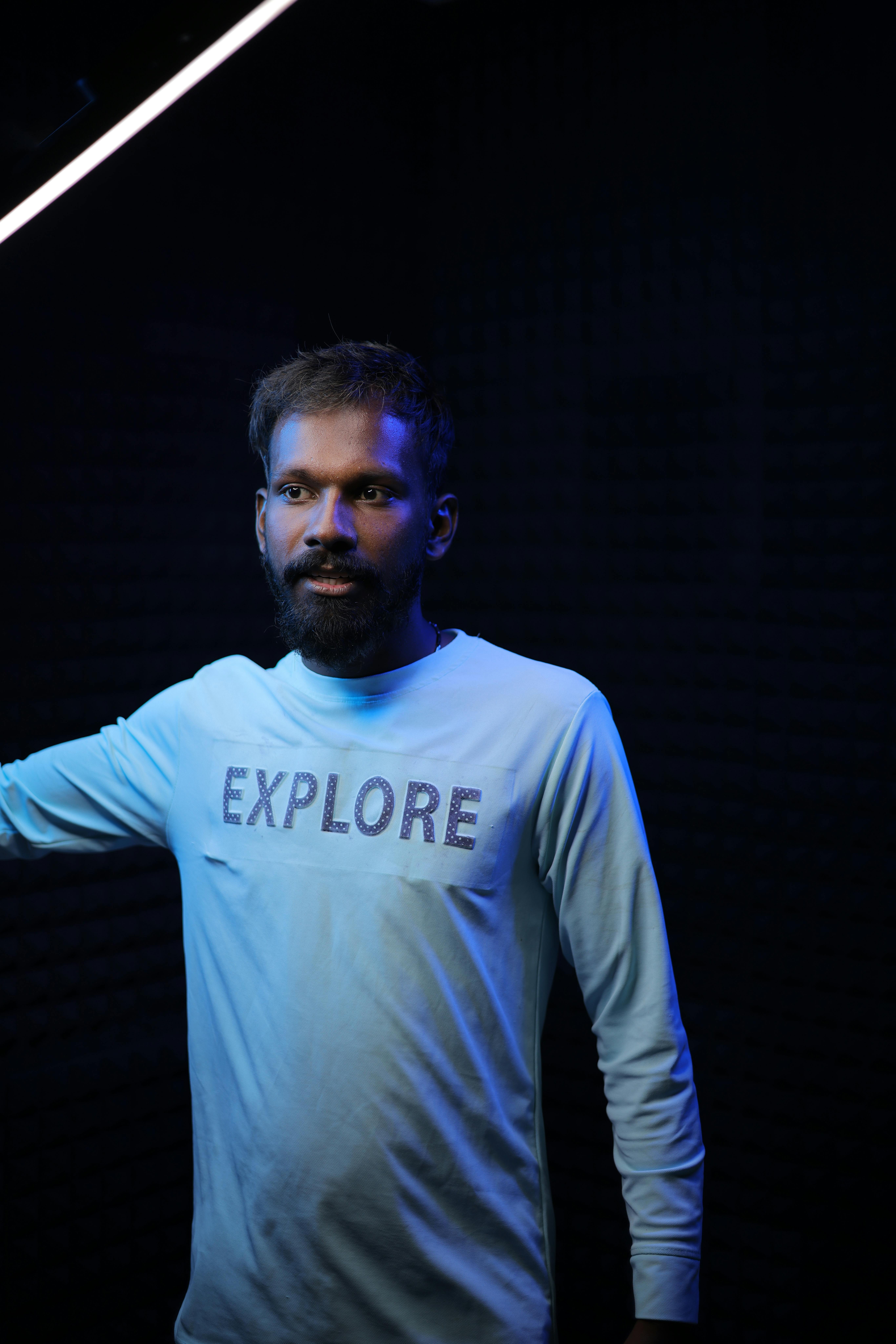 Man with a beard in white 'Explore' shirt, studio portrait.