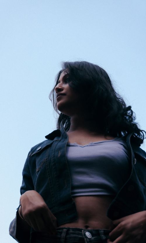 Free Portrait of a young woman in a denim jacket standing outdoors against a clear sky. Stock Photo