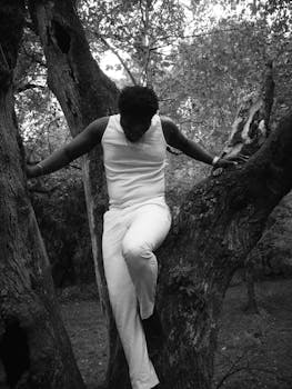 Stylish black and white portrait of a man in white clothing climbing a tree in an Atlanta forest.