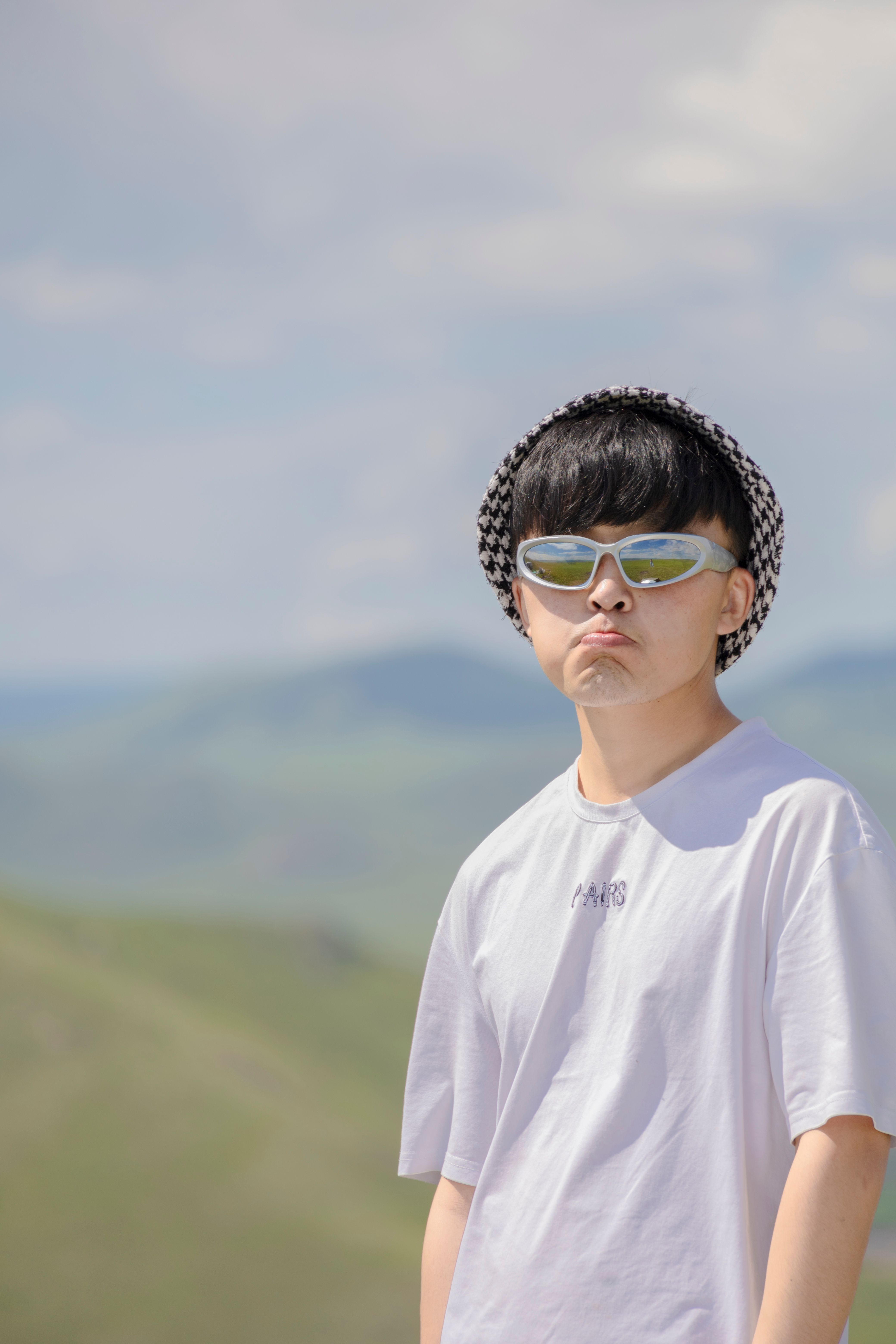Outdoor portrait of a young man with sunglasses and a hat against a scenic backdrop.