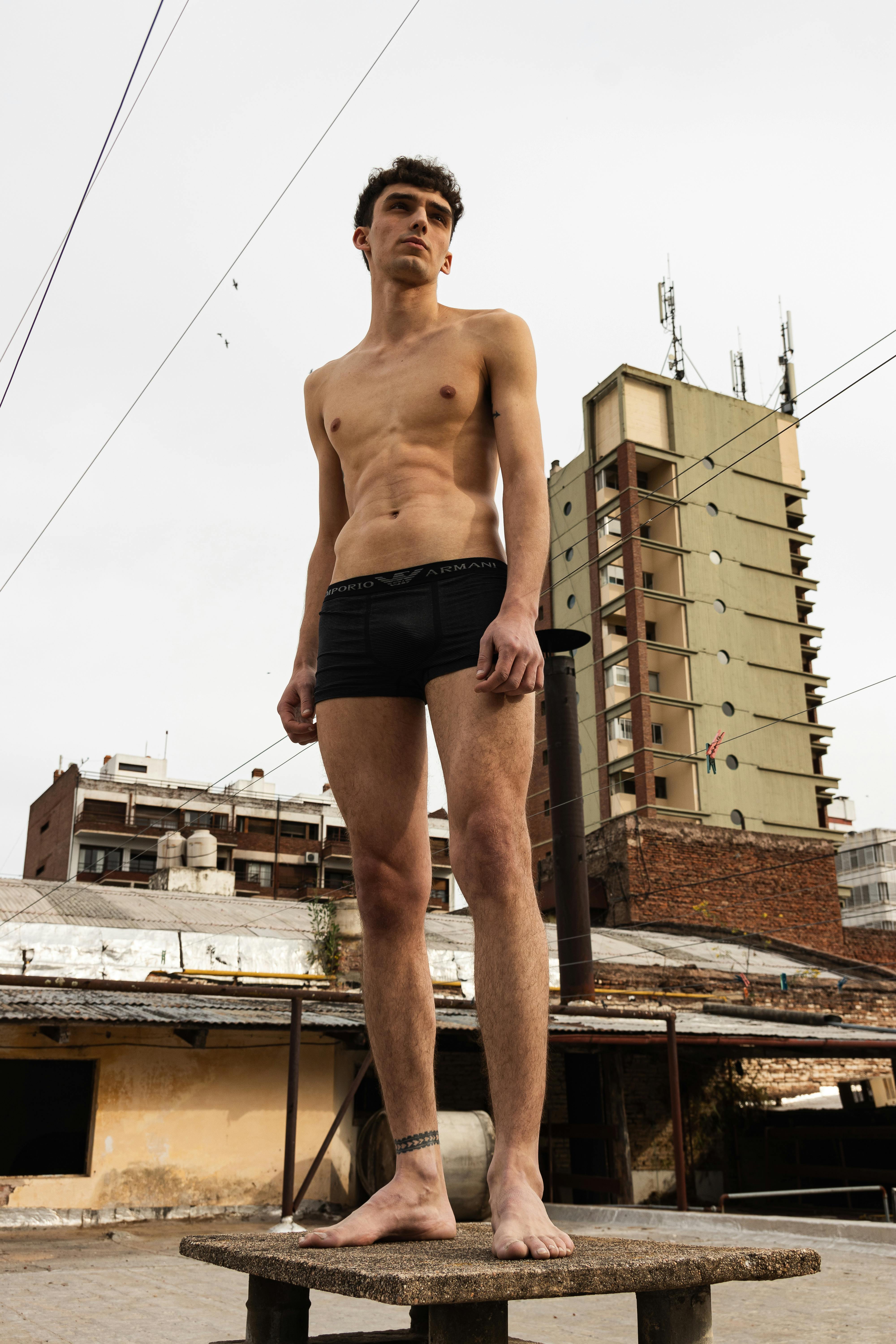 Young man in shorts posing on rooftop in urban setting. High-rise buildings, modern style, city vibes.