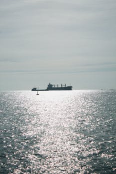 A solitary cargo ship sails across a sparkling ocean under a vast sky, creating a serene seascape.