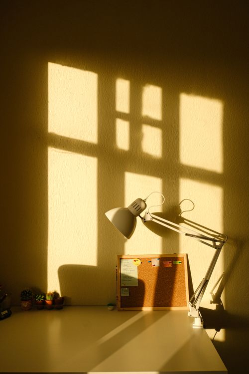 Free An artistic desk setup featuring a lamp casting shadows and a cork board in warm lighting. Stock Photo