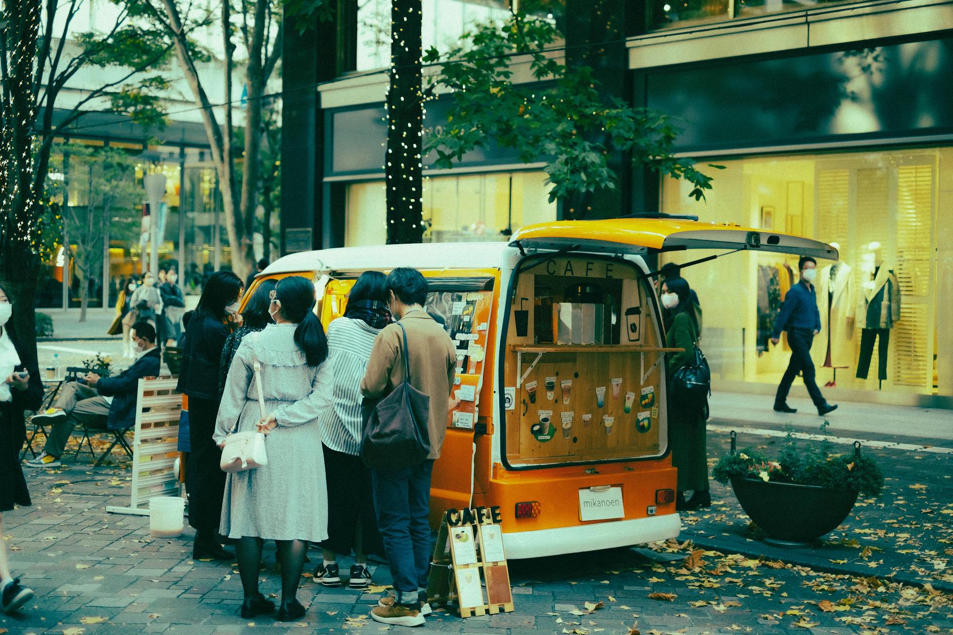 A vibrant coffee van with a queue of customers on a city street in autumn.