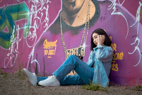 Young Woman in a Denim Jacket and Jeans Sitting Against a Wall with Graffiti
