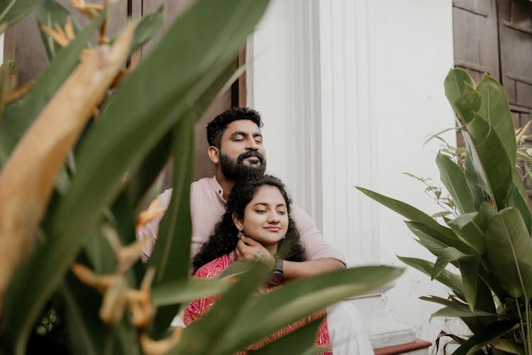 Man Hugging Woman Standing Among Plants From Behind