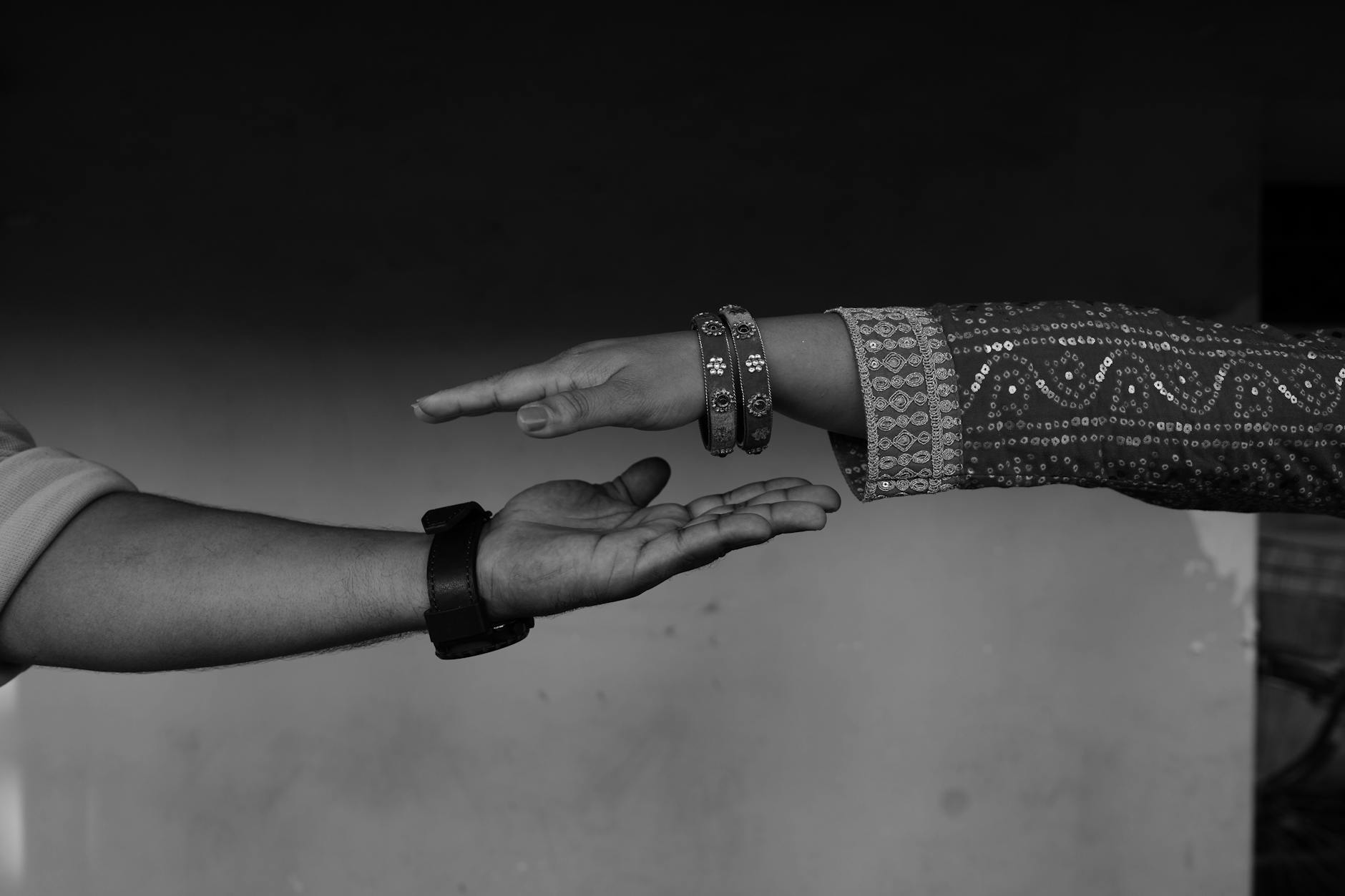 Black and white close-up of a man and woman reaching out hands, symbolizing connection.